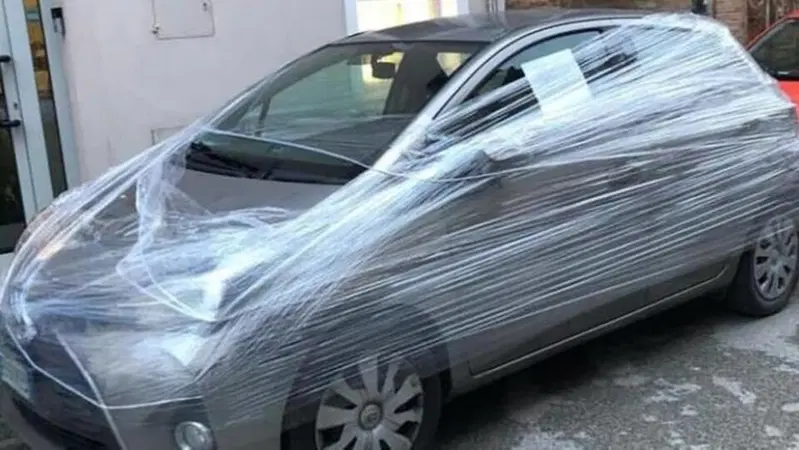 Incarta con il cellophane l'auto parcheggiata davanti al suo negozio